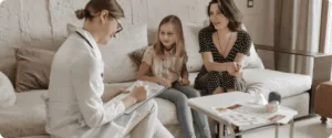 A Female Doctor Sitting Next To A Young Girl And Her Mother